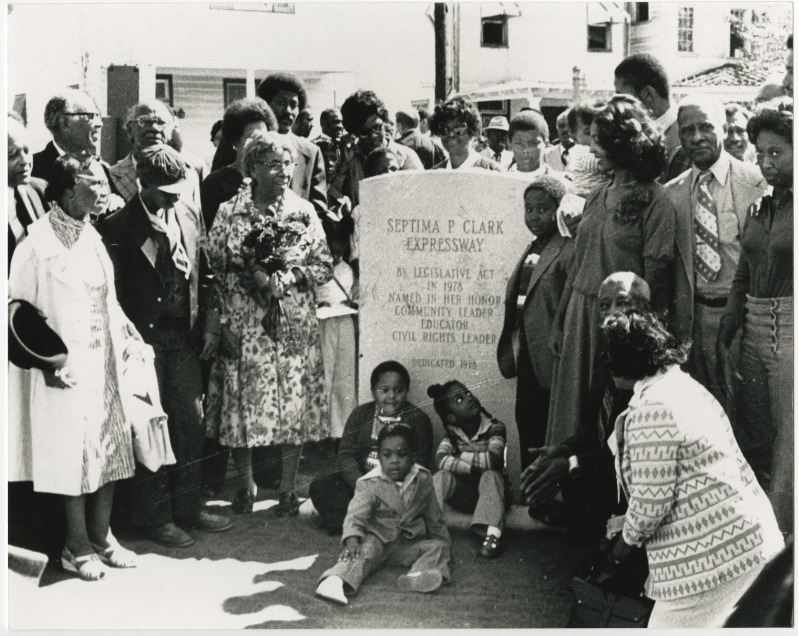 Black and white photograph of Septima P. Clark holding flowers with a large crowd around the Septima P. Clark Expressway stone marker.