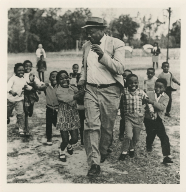 Black and white photograph of Esau Jenkins gathering with kids, John's Island 1960s. 